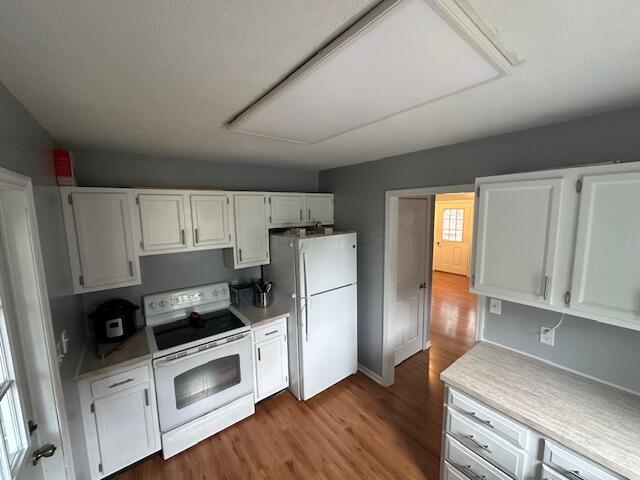 kitchen with white appliances, hardwood / wood-style flooring, and white cabinetry