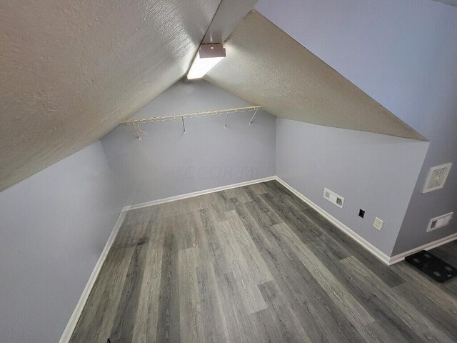 additional living space featuring a textured ceiling, dark hardwood / wood-style floors, and lofted ceiling