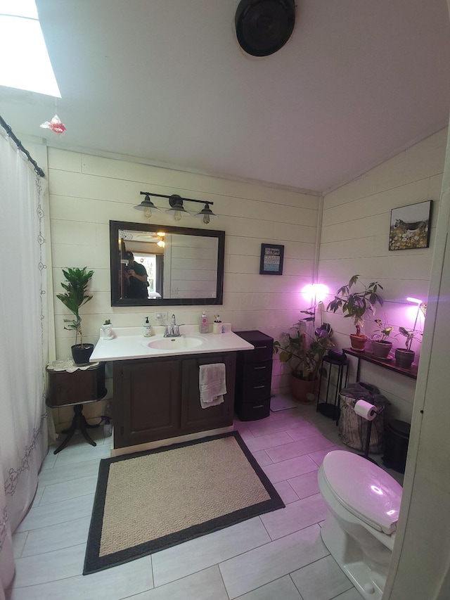 bathroom with toilet, vanity, vaulted ceiling, and tile patterned flooring