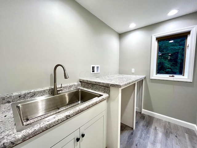 kitchen featuring white cabinets, light wood-type flooring, light stone counters, and sink