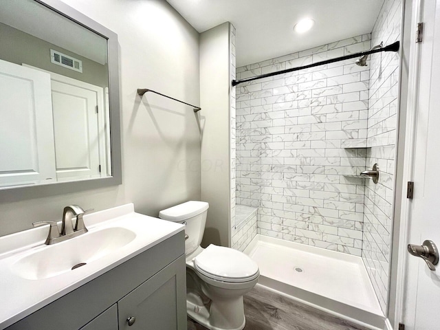 bathroom featuring tiled shower, vanity, hardwood / wood-style flooring, and toilet