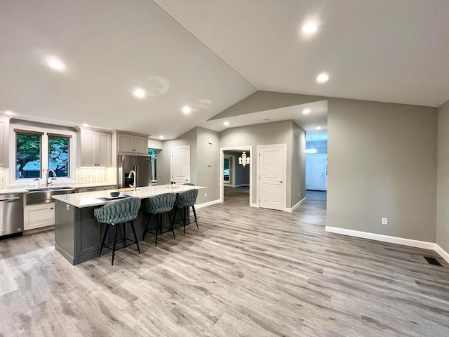 kitchen with light wood-type flooring, stainless steel appliances, a kitchen island with sink, sink, and lofted ceiling