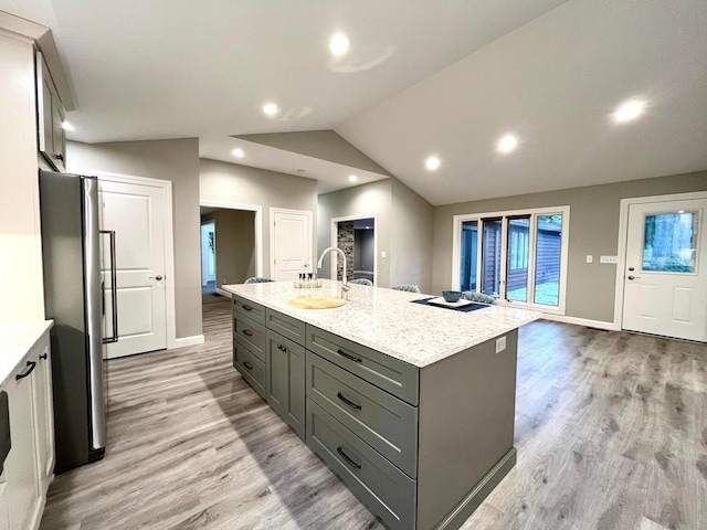 kitchen featuring stainless steel fridge, a center island with sink, vaulted ceiling, and light hardwood / wood-style flooring