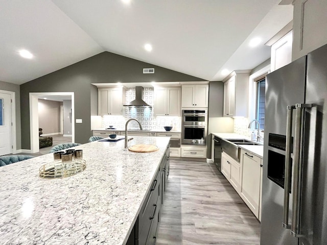 kitchen with sink, stainless steel appliances, light stone counters, wood-type flooring, and lofted ceiling