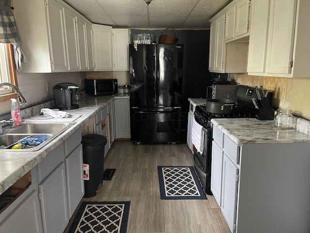 kitchen with stainless steel range, a drop ceiling, sink, black fridge, and light wood-type flooring