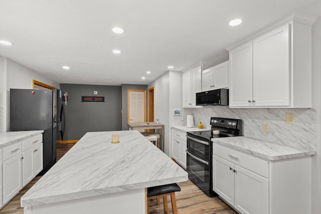 kitchen featuring light wood-type flooring, a center island, white cabinetry, and black appliances