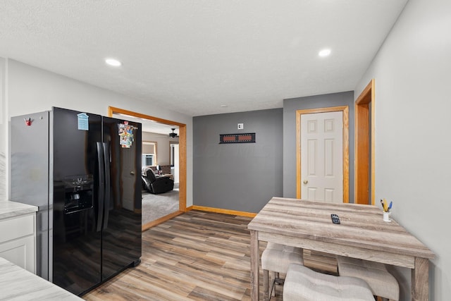 kitchen featuring white cabinets, black fridge, light hardwood / wood-style flooring, ceiling fan, and a textured ceiling