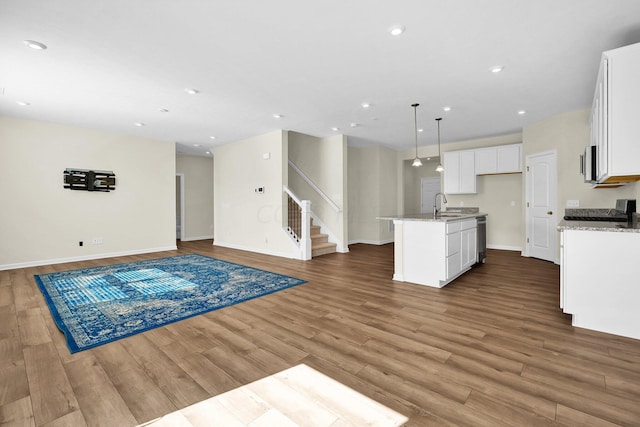 kitchen with light stone countertops, sink, a center island with sink, hardwood / wood-style flooring, and white cabinets