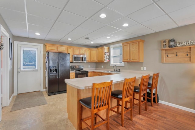 kitchen with kitchen peninsula, a kitchen breakfast bar, black appliances, light brown cabinets, and light hardwood / wood-style flooring