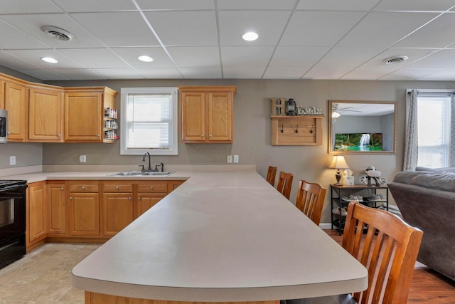 kitchen with light tile patterned flooring, black stove, a drop ceiling, and sink