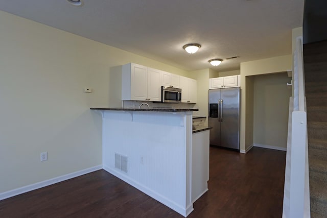 kitchen with visible vents, appliances with stainless steel finishes, white cabinets, a peninsula, and baseboards