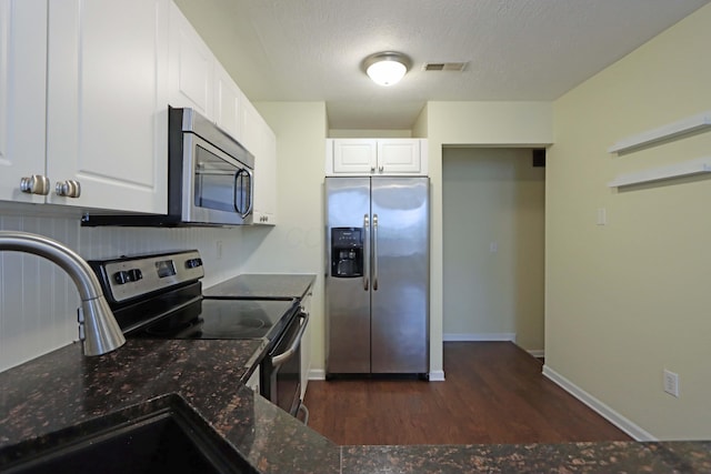 kitchen with visible vents, white cabinets, dark stone countertops, stainless steel appliances, and a sink