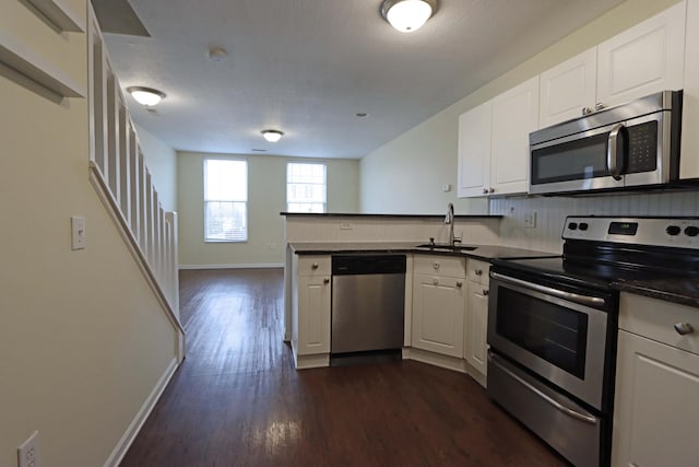 kitchen featuring dark countertops, dark wood-style floors, a peninsula, stainless steel appliances, and a sink