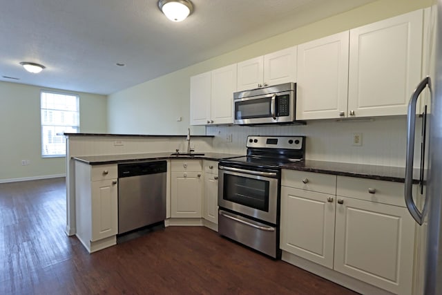 kitchen with appliances with stainless steel finishes, white cabinets, a peninsula, and dark wood-type flooring