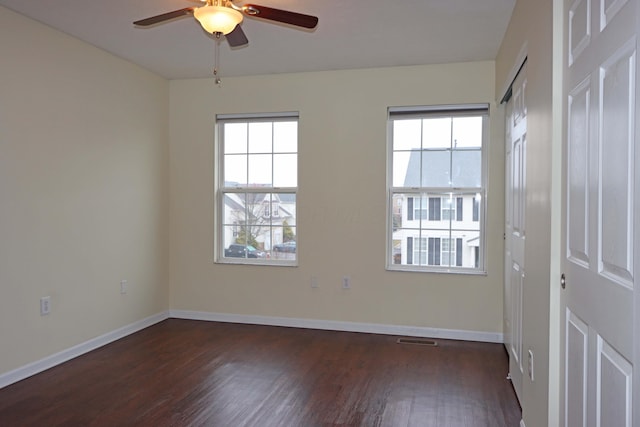 spare room featuring dark wood-style floors, a healthy amount of sunlight, visible vents, and baseboards