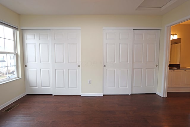 unfurnished bedroom with dark wood-style flooring, visible vents, multiple windows, and two closets