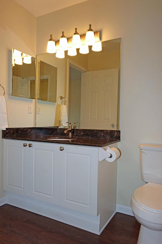 bathroom featuring toilet, baseboards, wood finished floors, and vanity