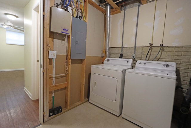 laundry area with light wood-type flooring, washing machine and dryer, electric panel, and baseboards