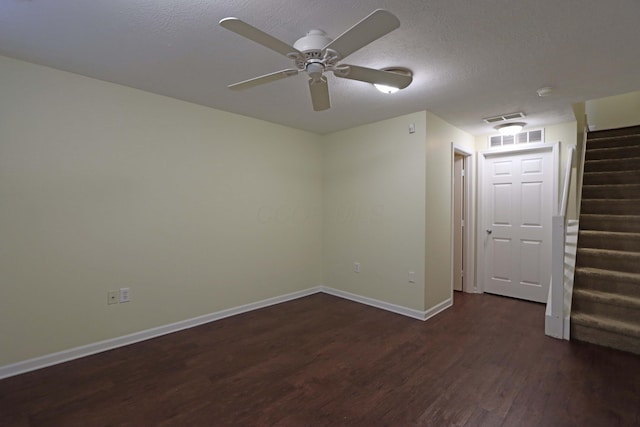 unfurnished room with a textured ceiling, wood finished floors, visible vents, baseboards, and stairs