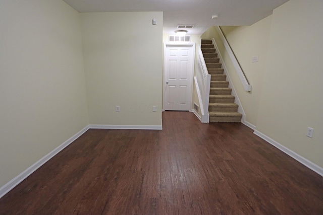 empty room featuring dark wood-style flooring, visible vents, baseboards, and stairs