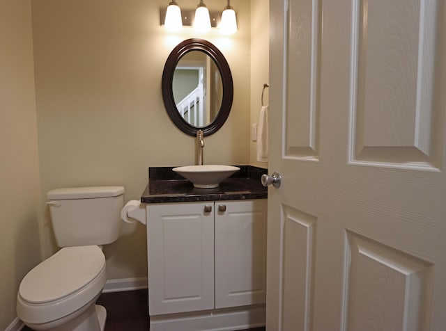 half bathroom featuring toilet, baseboards, and vanity