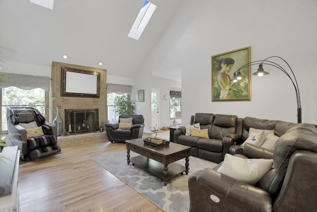 living room with a skylight, a fireplace, high vaulted ceiling, and light hardwood / wood-style flooring