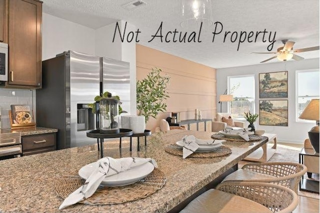 kitchen featuring light stone countertops, stainless steel fridge, backsplash, a textured ceiling, and ceiling fan