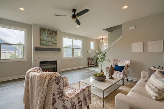 living room with a tile fireplace, ceiling fan, and light wood-type flooring