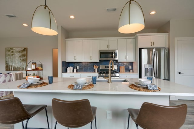 kitchen featuring pendant lighting, an island with sink, appliances with stainless steel finishes, and tasteful backsplash