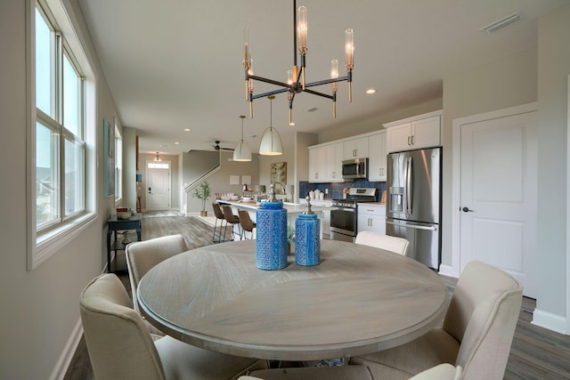 dining space featuring ceiling fan with notable chandelier and dark wood-type flooring