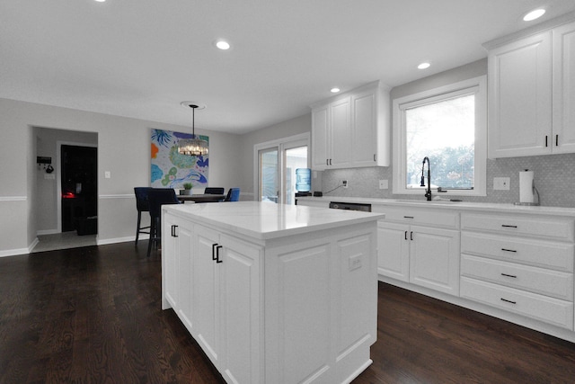 kitchen featuring backsplash, a kitchen island, sink, white cabinetry, and hanging light fixtures