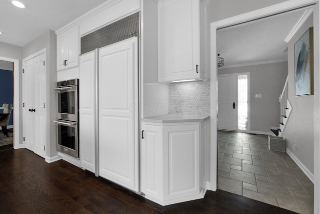 kitchen featuring white cabinets, crown molding, decorative backsplash, dark hardwood / wood-style floors, and double oven