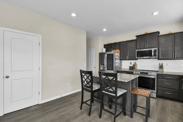 kitchen with light stone countertops, appliances with stainless steel finishes, a kitchen breakfast bar, dark hardwood / wood-style floors, and a kitchen island