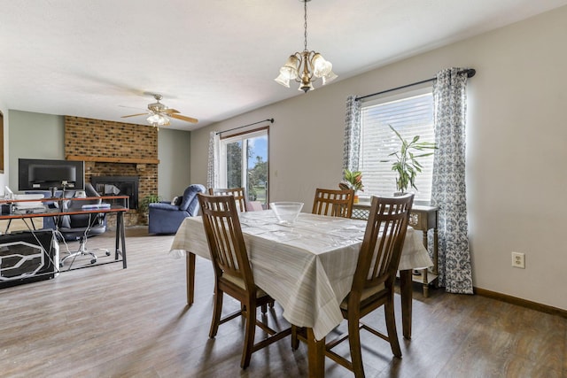 dining area featuring hardwood / wood-style floors, ceiling fan with notable chandelier, and a brick fireplace