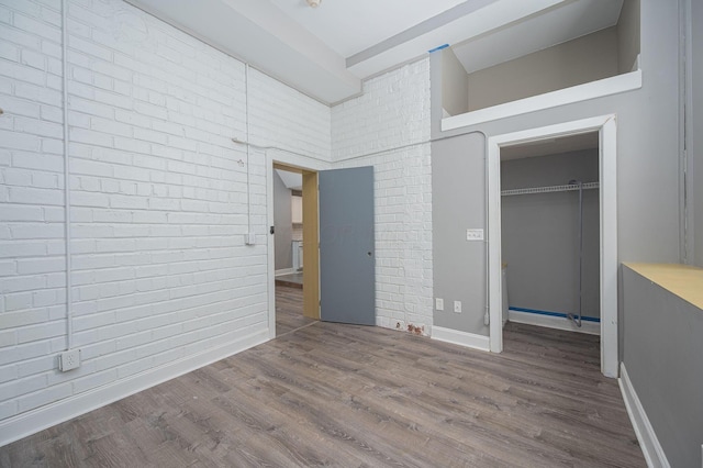 unfurnished bedroom with hardwood / wood-style floors, a closet, a high ceiling, and brick wall