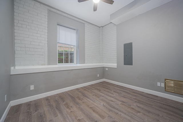 spare room featuring hardwood / wood-style flooring, ceiling fan, brick wall, and electric panel