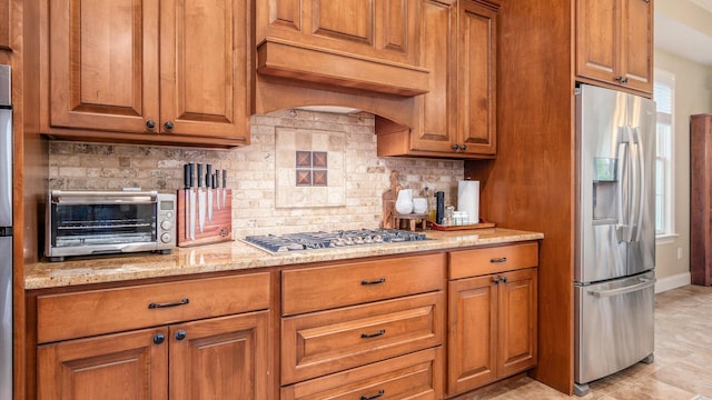 kitchen with custom range hood, backsplash, stainless steel appliances, and light stone counters