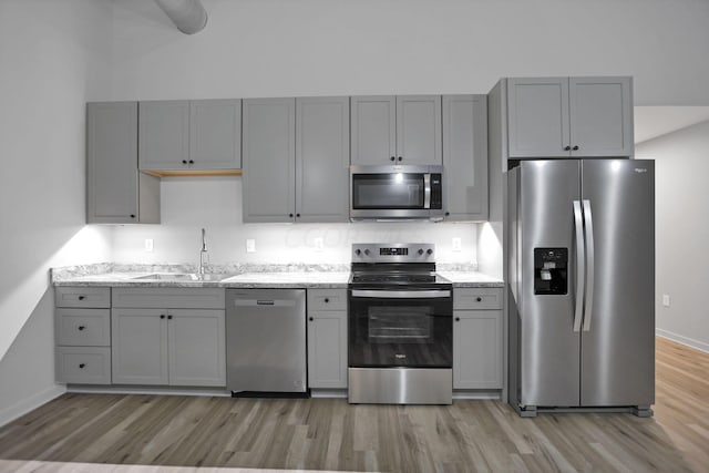 kitchen featuring light stone countertops, appliances with stainless steel finishes, sink, light hardwood / wood-style flooring, and gray cabinets