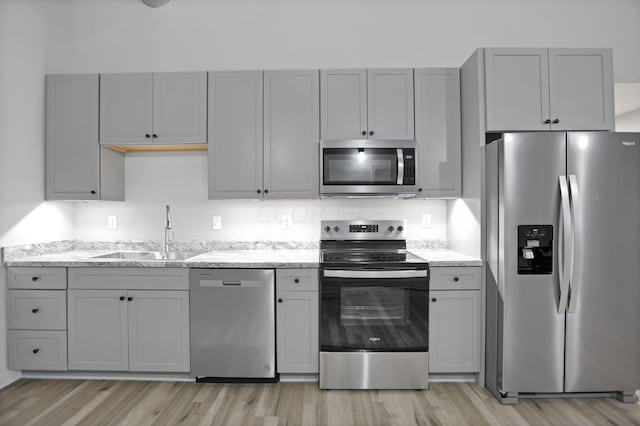 kitchen featuring gray cabinetry, sink, light wood-type flooring, appliances with stainless steel finishes, and light stone counters