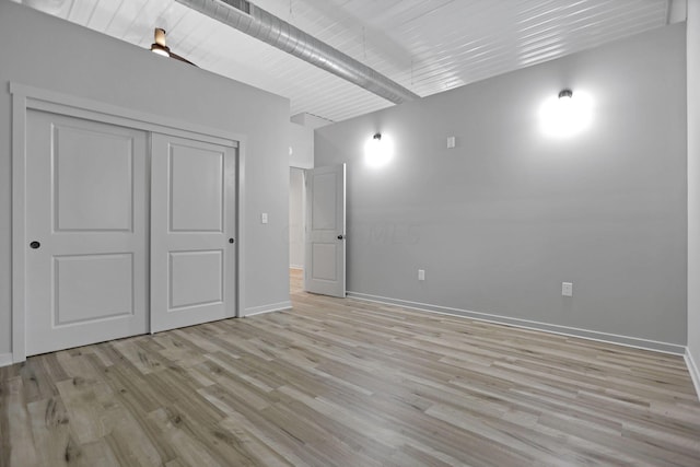 unfurnished bedroom featuring light hardwood / wood-style floors, beam ceiling, and a closet