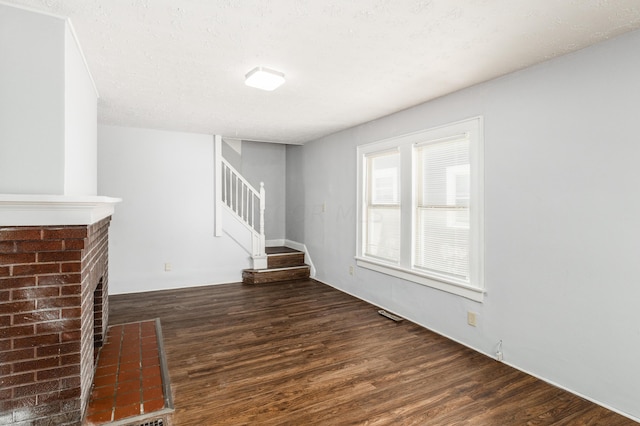 unfurnished living room featuring a fireplace, dark hardwood / wood-style flooring, and a textured ceiling