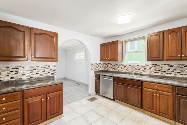 kitchen with decorative backsplash, stainless steel dishwasher, sink, light tile patterned floors, and dark stone countertops