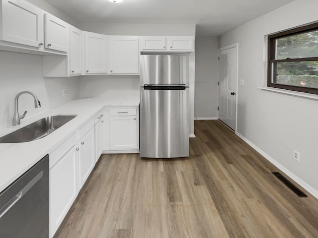 kitchen with white cabinets, appliances with stainless steel finishes, light hardwood / wood-style floors, and sink