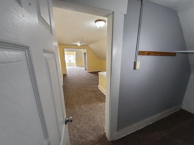 hallway with dark colored carpet, lofted ceiling, and a textured ceiling