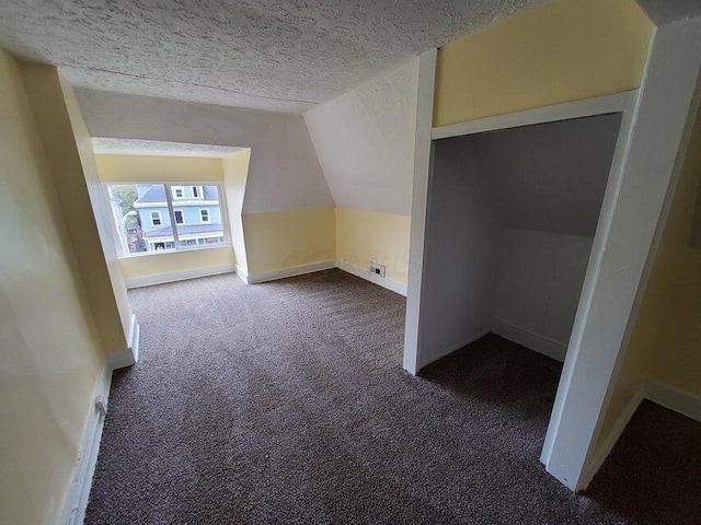 additional living space with a textured ceiling, dark carpet, and lofted ceiling