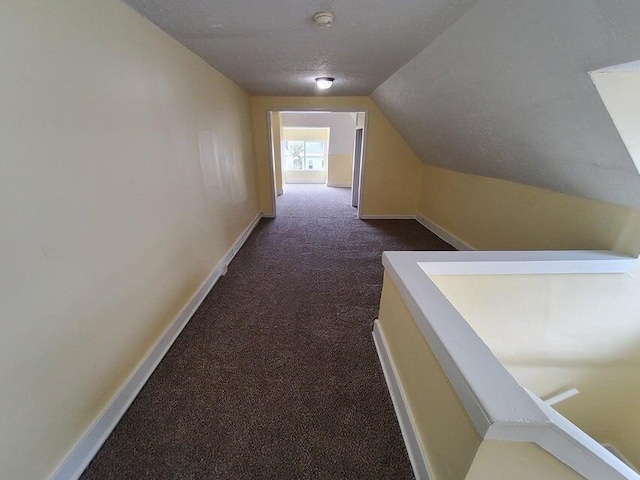 hall featuring dark colored carpet, lofted ceiling, and a textured ceiling