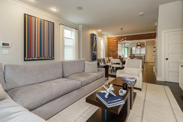 living room featuring crown molding, brick wall, a notable chandelier, and hardwood / wood-style flooring