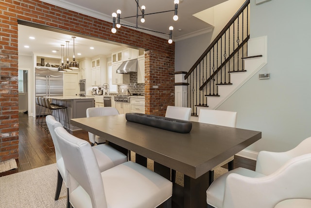 dining area featuring dark hardwood / wood-style flooring, a notable chandelier, ornamental molding, and brick wall