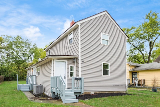 back of property with central AC and a lawn