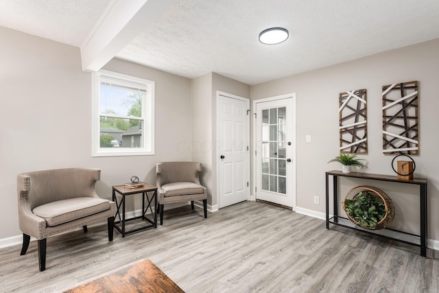 living area with beam ceiling, light hardwood / wood-style flooring, and a textured ceiling